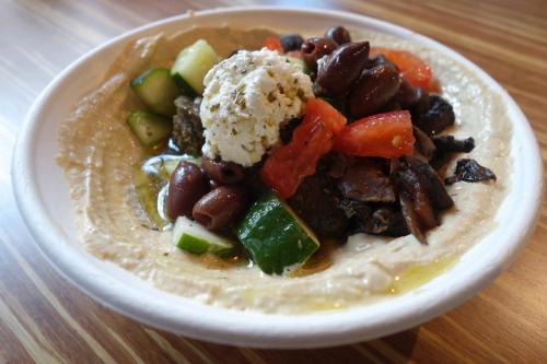 Photo of original hummus topped with a squirt of olive oil, falafel, mushrooms, cucumbers, tomatoes, olives, feta cheese and a swirl of the lemon-mint vinaigrette.